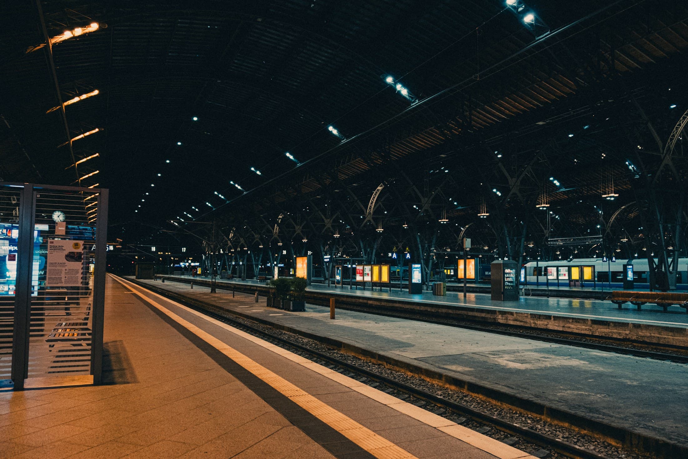 An empty railway platform beneath a high roof at night.